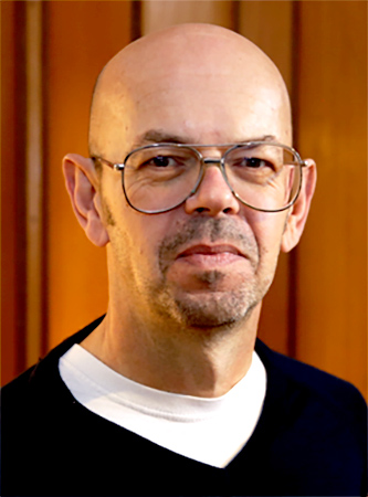 Porträtfoto von Ulf Treger, frontal, im blauen Pullover vor einer Holzwand